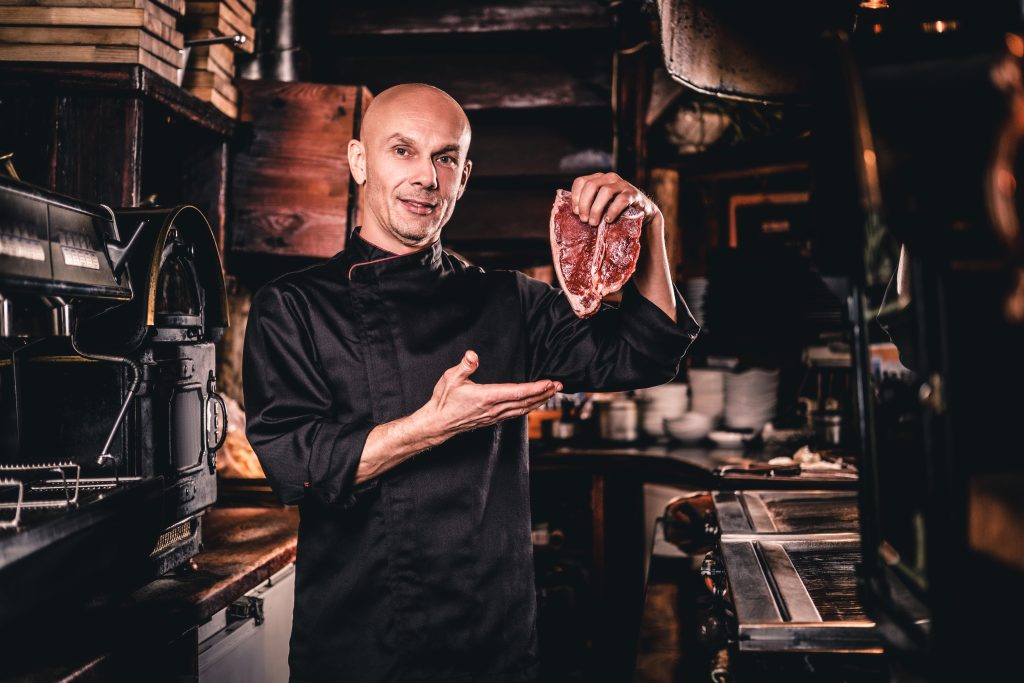 confident chef wearing uniform presenting fresh steak before cooking looking camera restaurant kitchen
